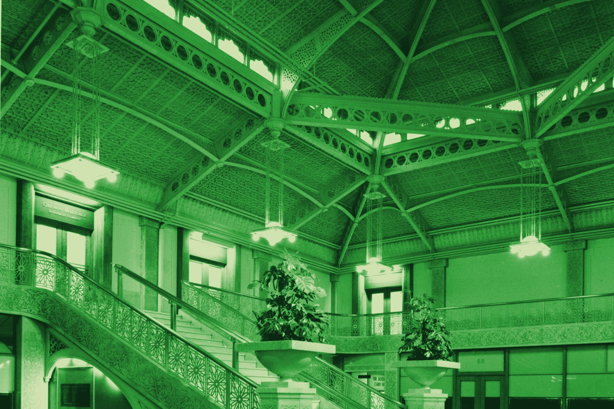 Upward view inside a grand institutional atrium, a glass-vaulted ceiling over a marble staircase.
