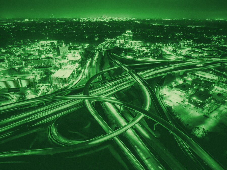 Aerial night view of a tangled multi-lane urban highway interchange.
